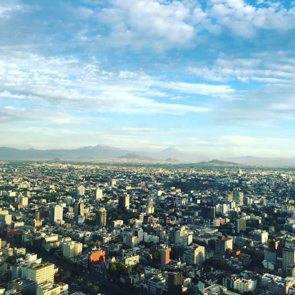 Aerial view of Mexico City with high-rise buildings, mountains, and a wide blue sky.