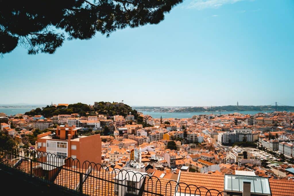 View over Lisbon rooftops, hills, and the Tagus River on a sunny day.