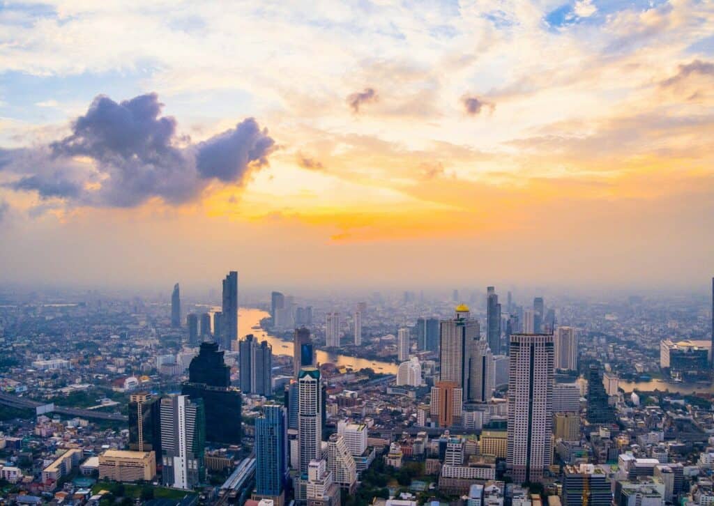Bangkok skyline at sunset with high-rise buildings, river views, and warm evening light.