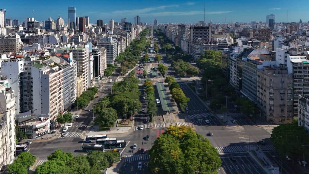 Aerial view of Buenos Aires with a wide tree-lined avenue, city buildings, and clear blue sky.