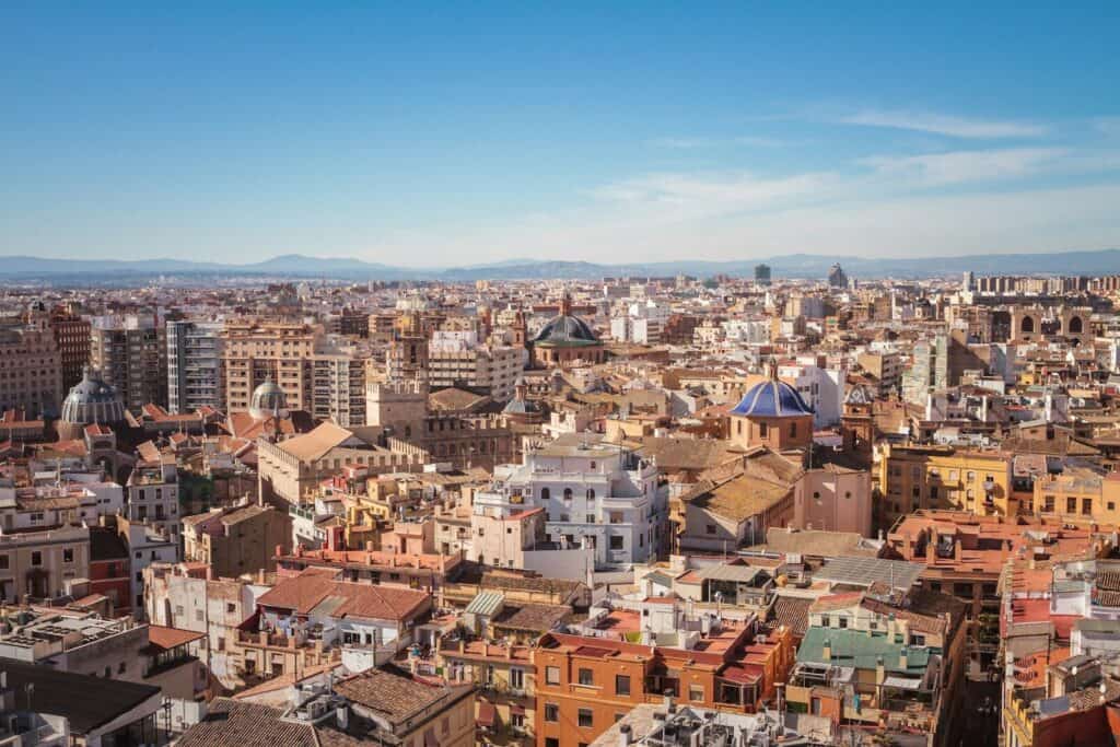 View over Valencia rooftops with historic buildings, domes, and a clear blue sky.