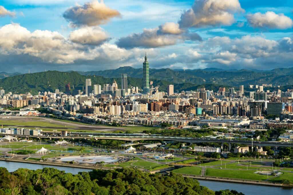 Taipei skyline with Taipei 101, city buildings, green hills, and dramatic clouds.