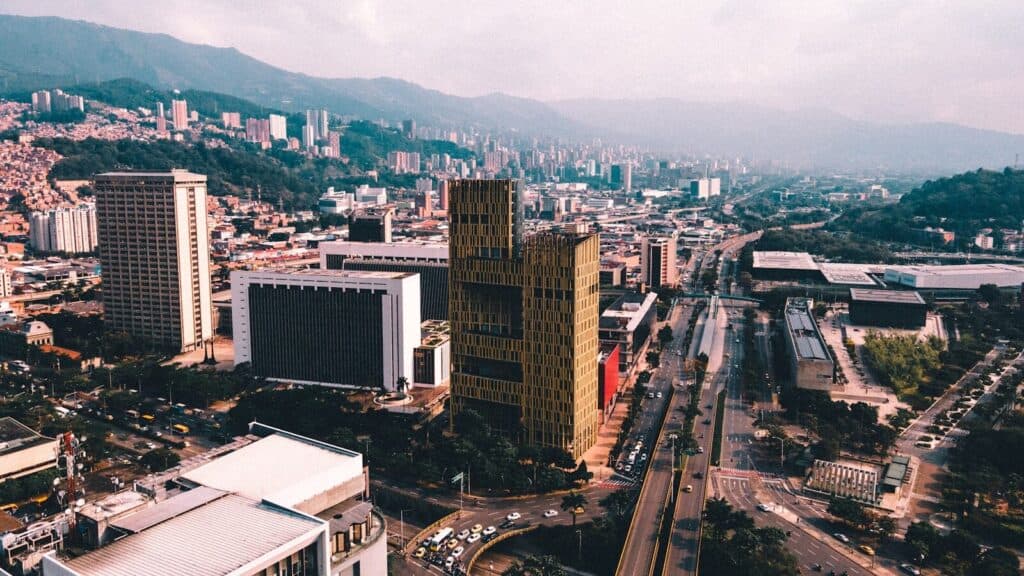 Aerial view of Medellin with modern buildings, wide roads, and mountains around the city.