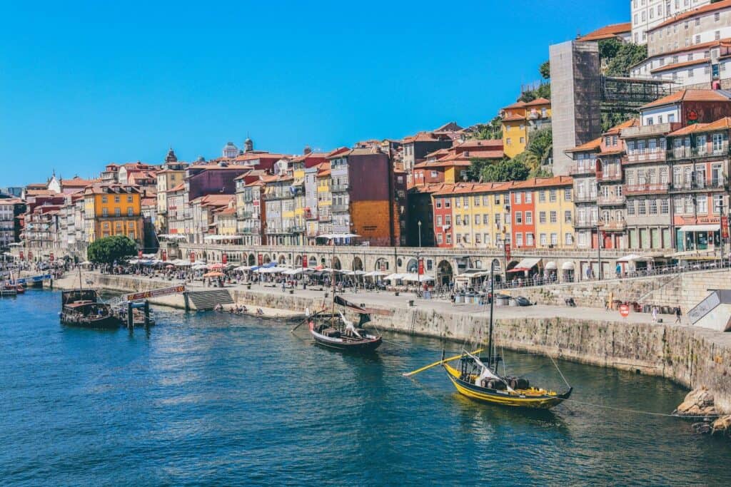View of Porto’s riverside with colorful buildings, boats, and blue water on a sunny day.