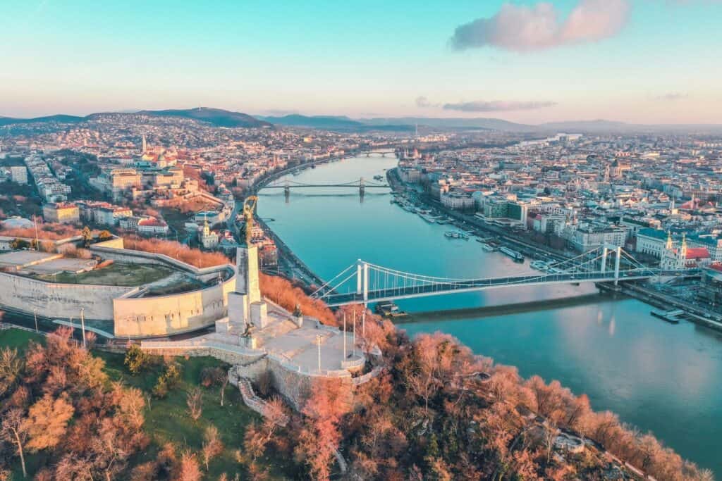 Aerial view of Budapest with the Danube River, bridges, and city skyline in soft evening light.